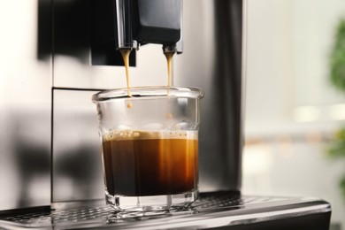 Photo of Espresso machine pouring coffee into glass against blurred background, closeup. Space for text