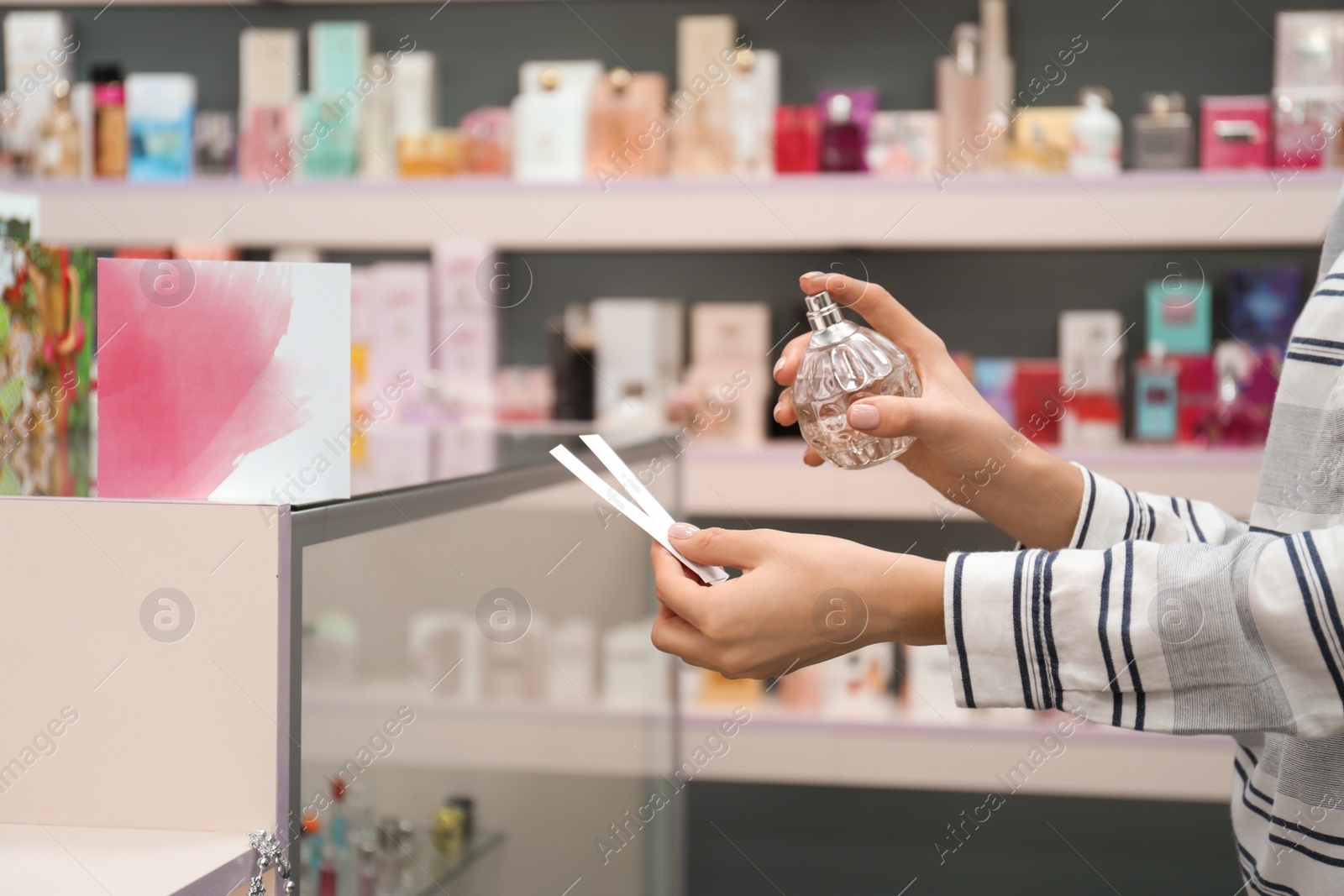 Photo of Young woman with bottle of perfume and blotters in shop, closeup