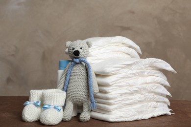 Baby diapers, toy bear and child's booties on wooden table