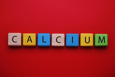 Photo of Word Calcium madecolorful wooden cubes with letters on red background, flat lay