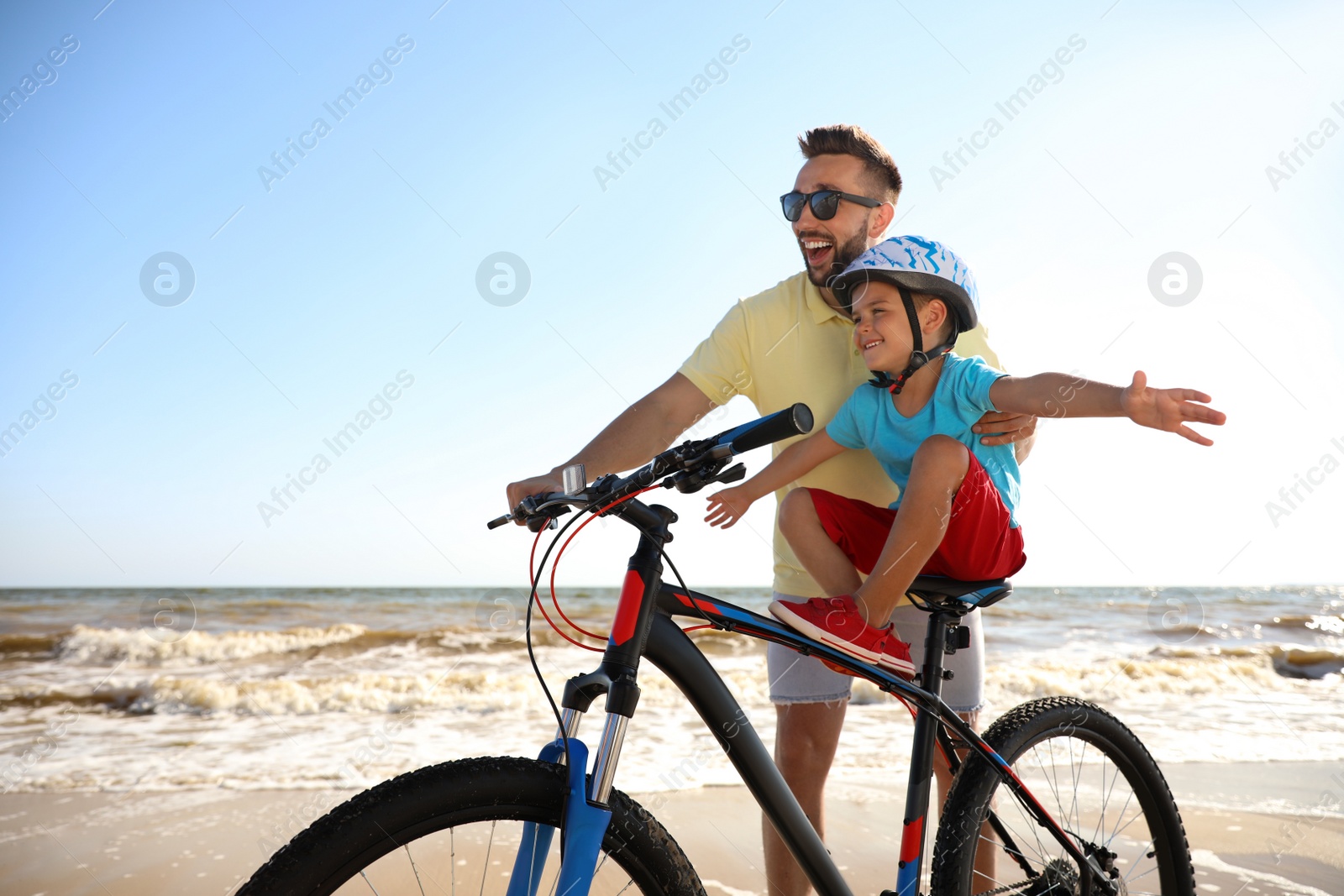 Photo of Happy father teaching son to ride bicycle on sandy beach near sea