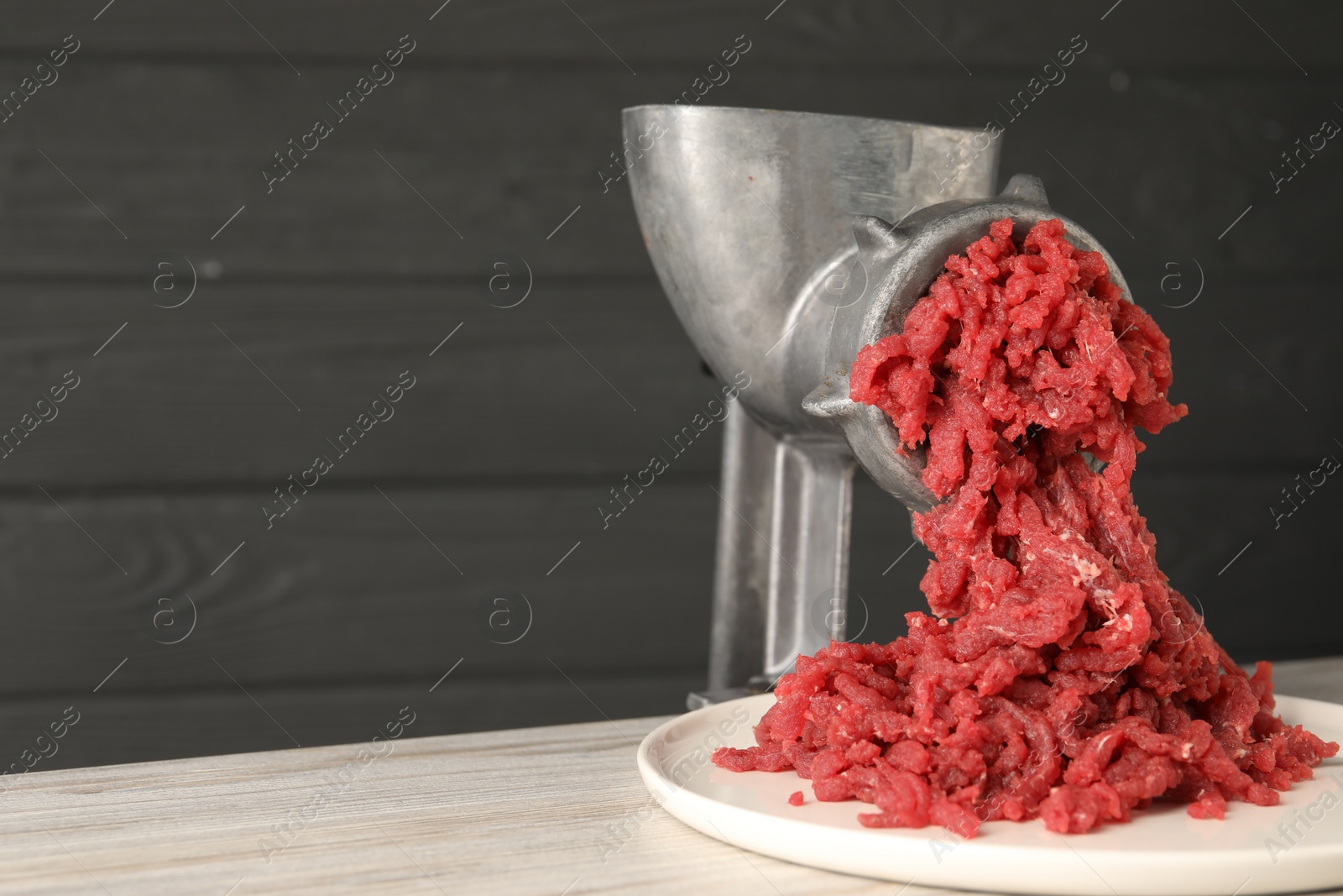Photo of Metal meat grinder with beef mince on table. Space for text