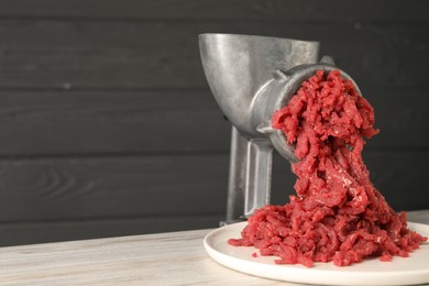 Metal meat grinder with beef mince on table. Space for text