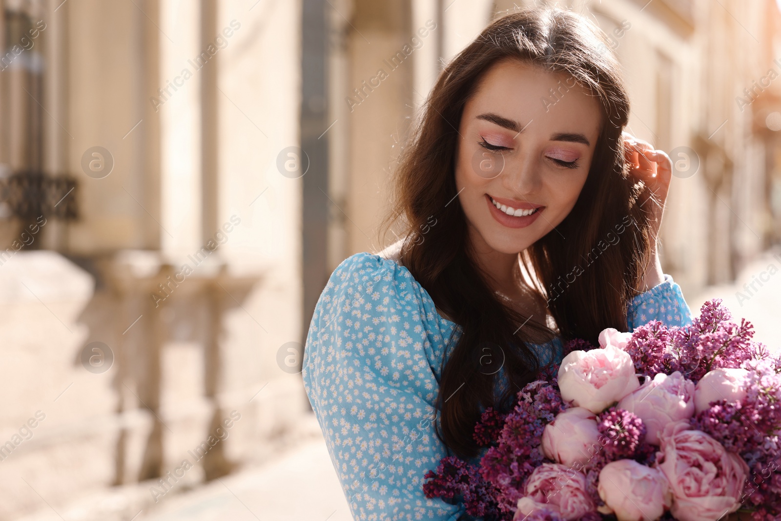 Photo of Beautiful woman with bouquet of spring flowers on city street, space for text