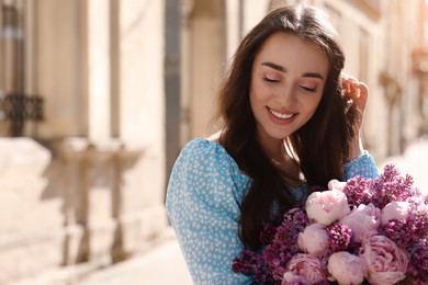 Beautiful woman with bouquet of spring flowers on city street, space for text