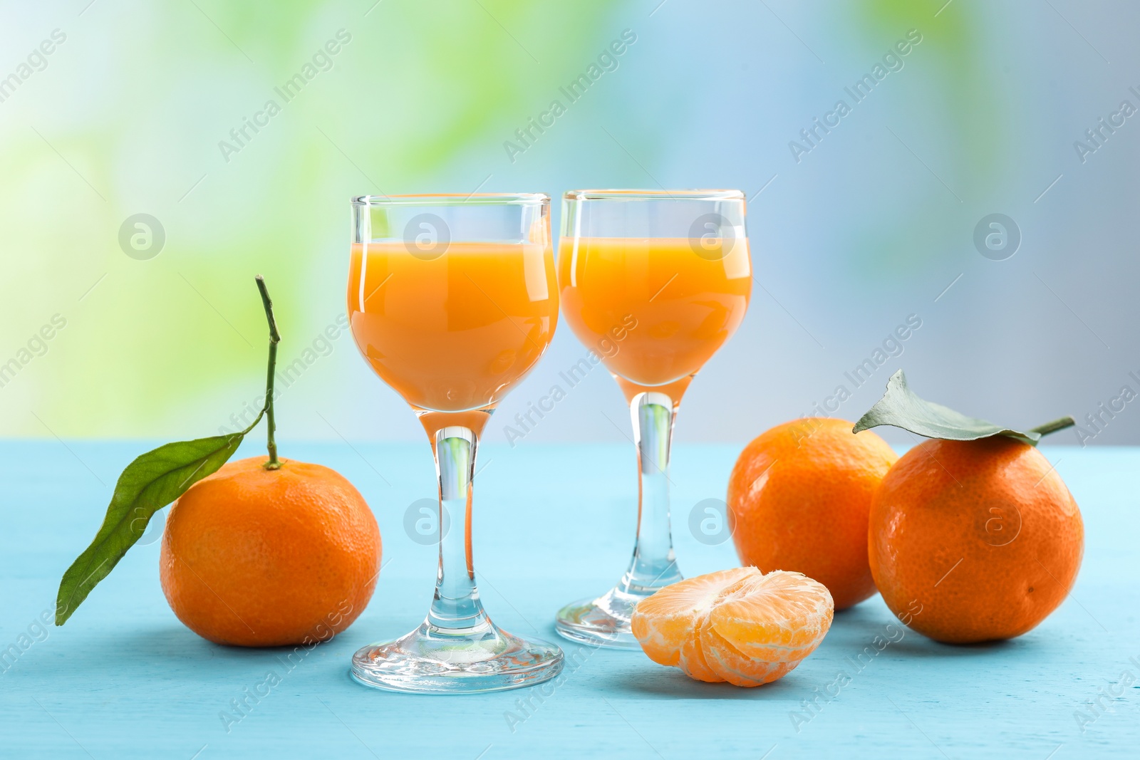 Photo of Delicious tangerine liqueur and fresh fruits on light blue wooden table