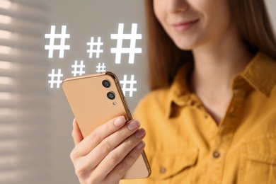 Woman using modern smartphone, closeup. Hashtag symbols over device