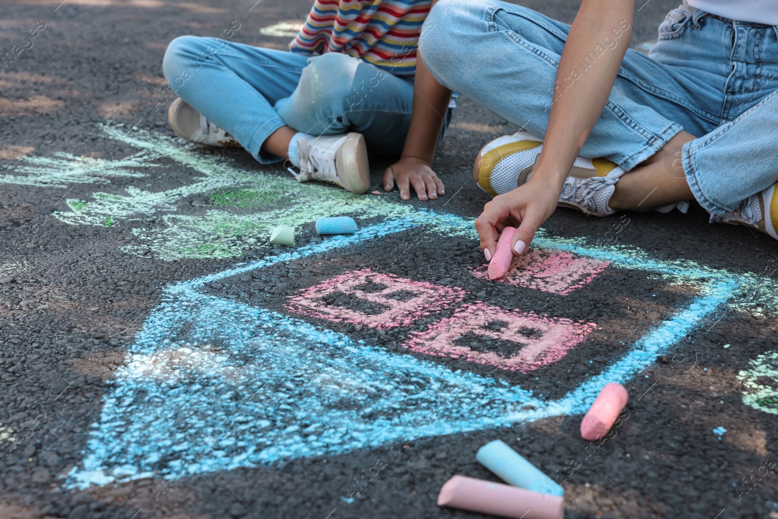 Photo of Little child and her mother drawing with colorful chalks on asphalt, closeup