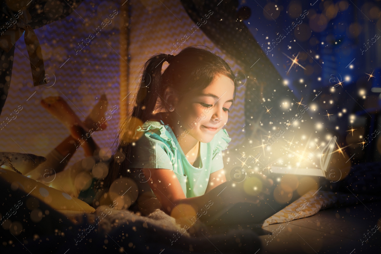 Image of Little girl reading fairy tale in play tent at home