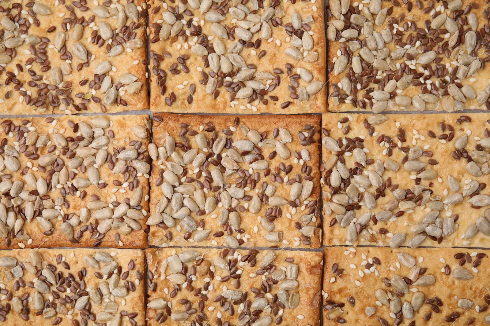 Photo of Cereal crackers with flax, sunflower and sesame seeds as background, top view