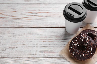 Tasty donuts and cups of hot drinks on white wooden table, above view. Space for text