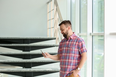 Photo of Portrait of handsome bearded man with mobile phone near stairs, indoors