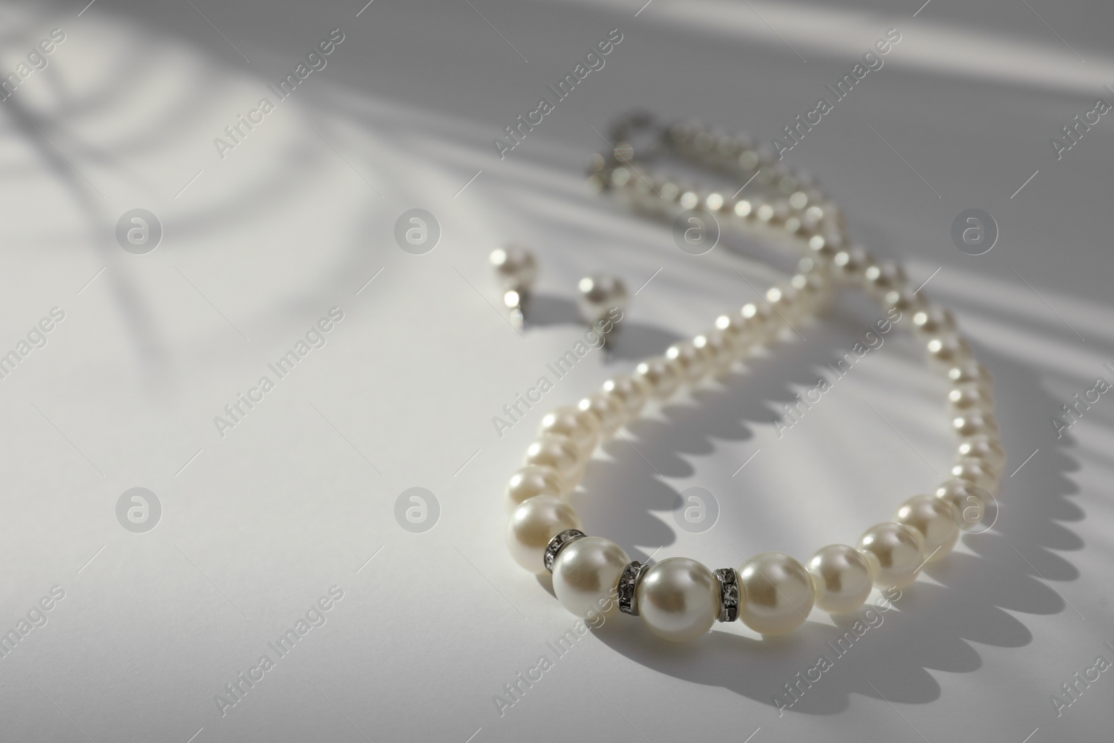 Photo of Elegant pearl necklace and earrings on white table, closeup. Space for text