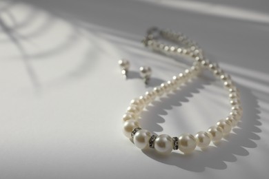 Photo of Elegant pearl necklace and earrings on white table, closeup. Space for text