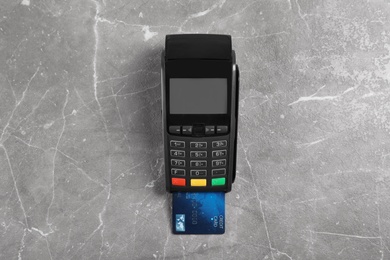 Photo of Modern payment terminal with credit card on grey background, top view