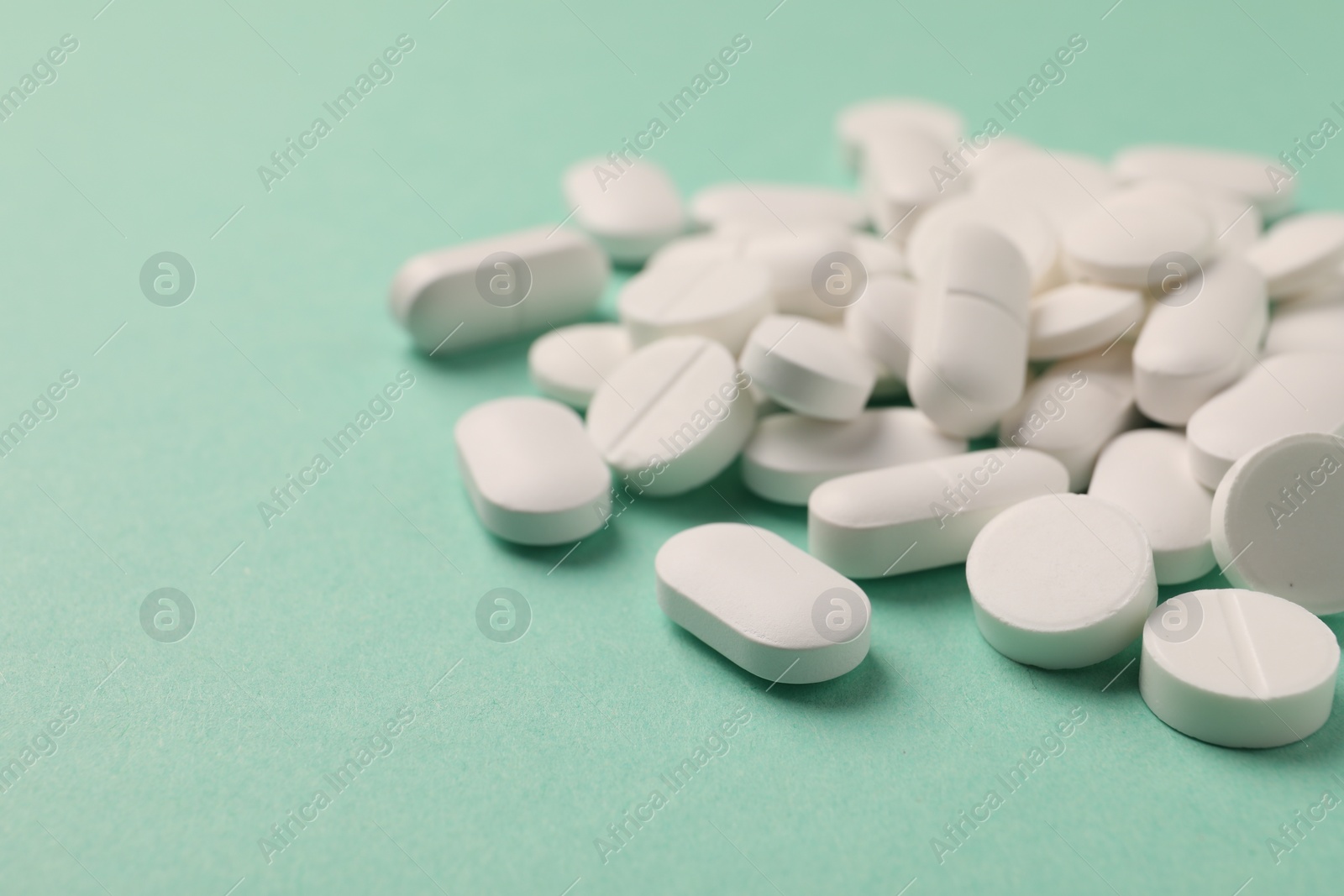Photo of Pile of white pills on green background, selective focus. Space for text