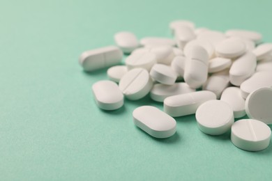 Pile of white pills on green background, selective focus. Space for text