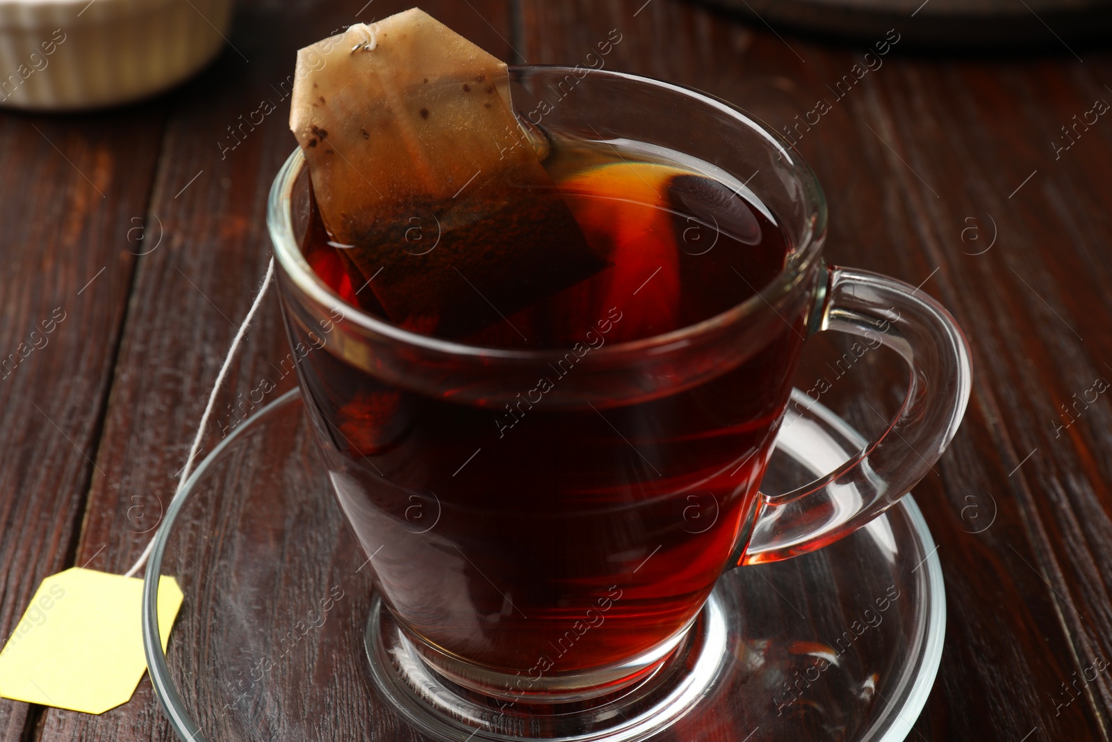 Photo of Brewing tea. Glass cup with tea bag on wooden table, closeup