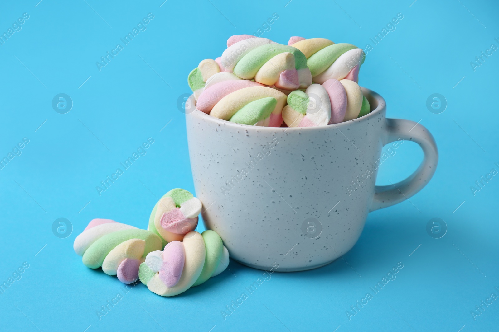 Photo of Cup with delicious colorful marshmallows on light blue background