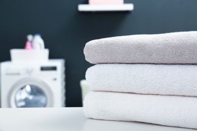 Stack of clean towels on table in laundry room, closeup. Space for text