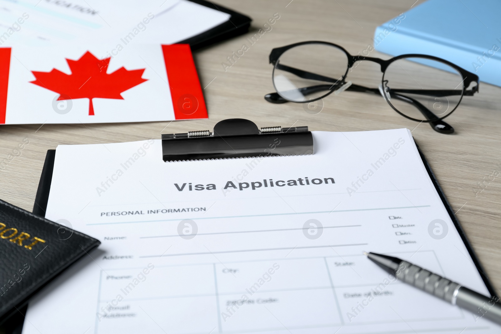 Photo of Visa application form for immigration, passport, Canadian flag and glasses on wooden table, closeup
