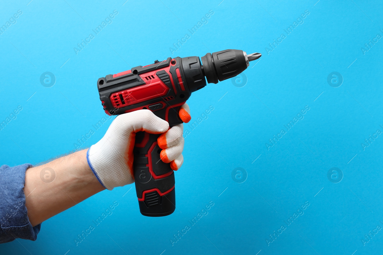 Photo of Handyman holding electric screwdriver on light blue background, closeup