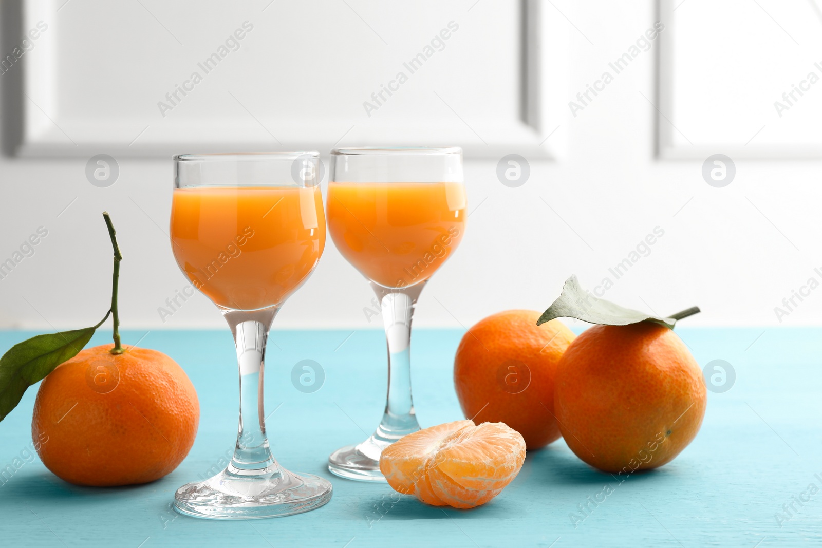 Photo of Delicious tangerine liqueur and fresh fruits on light blue wooden table
