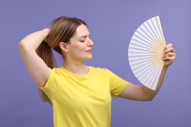 Beautiful woman waving hand fan to cool herself on violet background