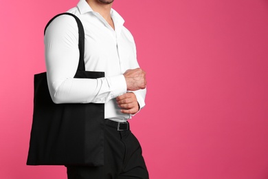 Photo of Young man holding black tote bag on pink background, closeup. Mockup for design