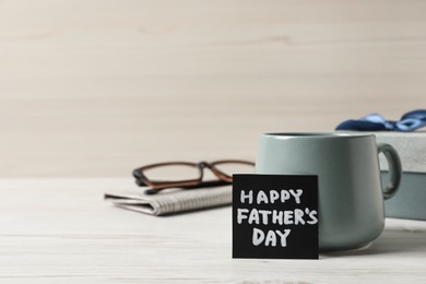 Photo of Card with phrase Happy Father's Day, cup of aromatic coffee, gift box and glasses on white wooden background. Space for text