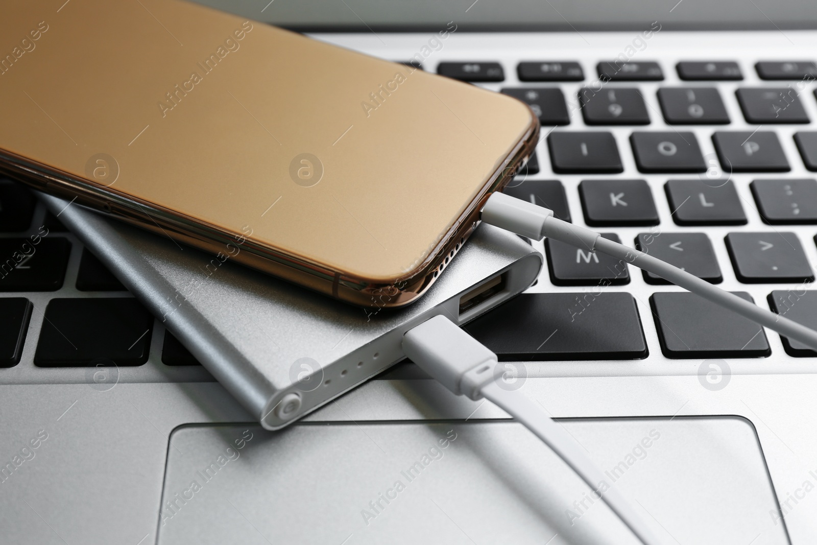 Photo of Modern smartphone charging with power bank on laptop, closeup