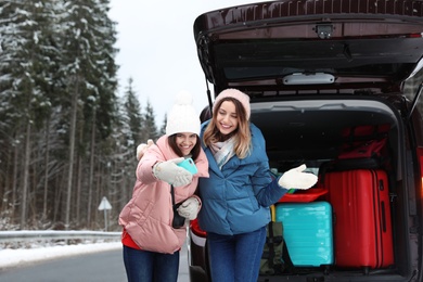 Photo of Friends taking selfie near open car trunk full of luggage on road. Winter vacation