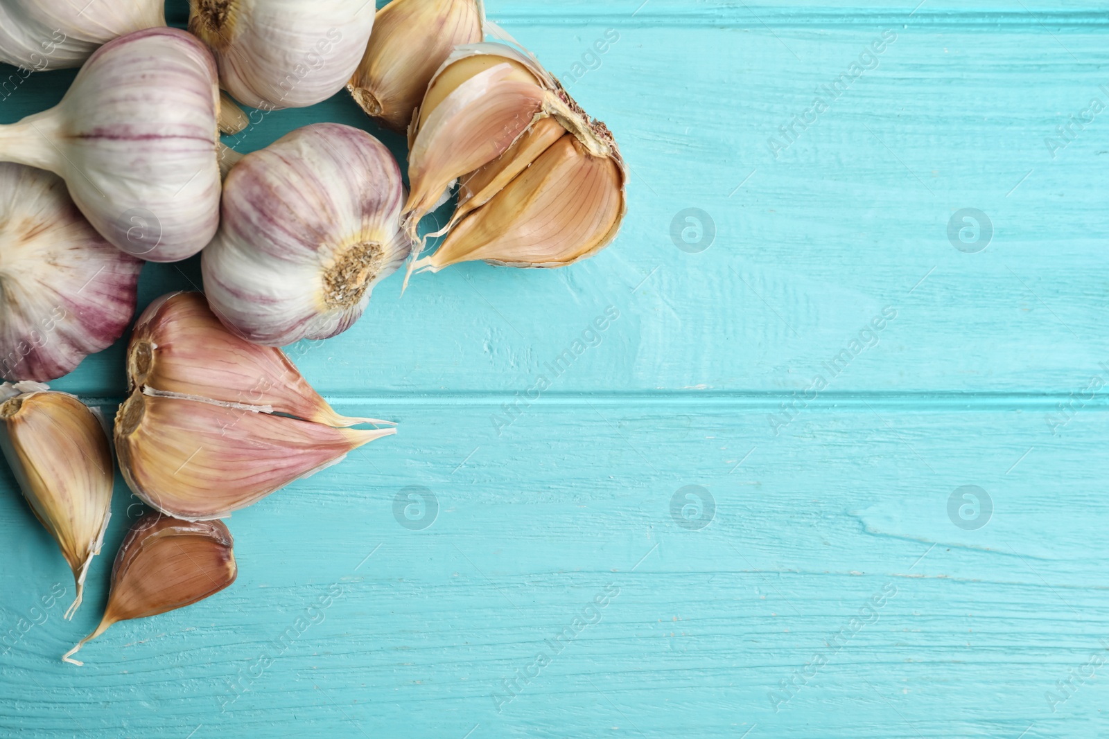 Photo of Fresh unpeeled garlic bulbs and cloves on light blue wooden table, flat lay with space for text. Organic product