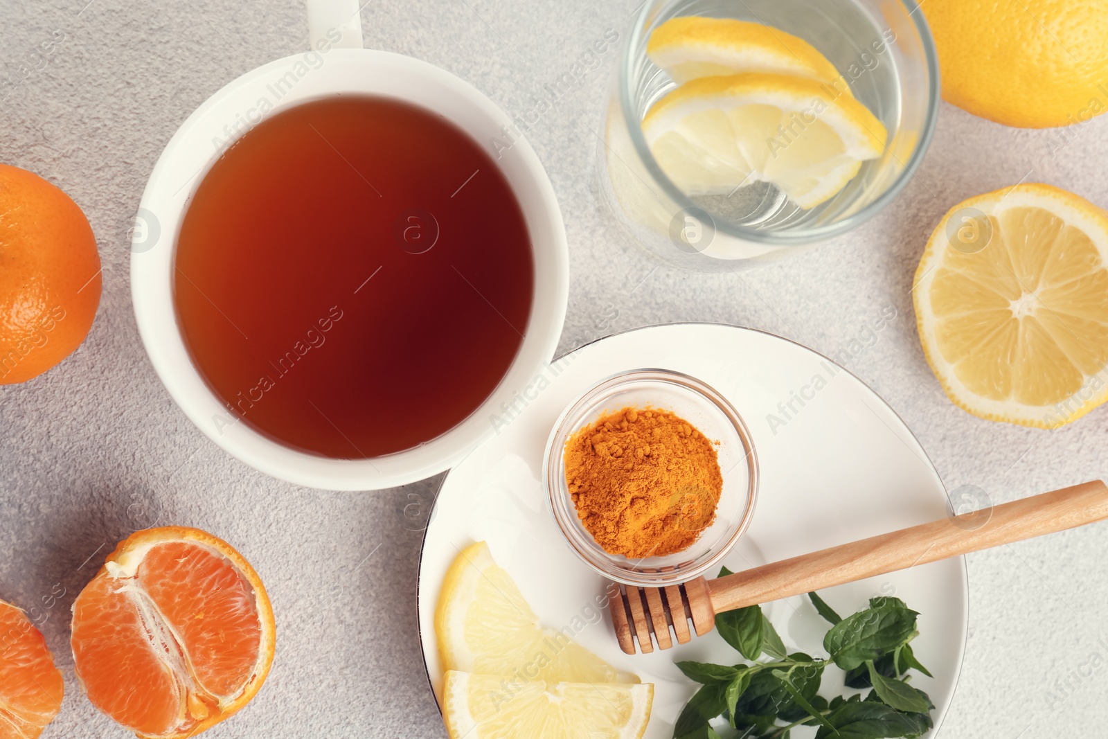 Photo of Cup of delicious immunity boosting tea with citrus fruits and turmeric on light grey table, flat lay