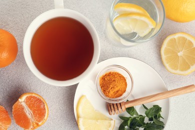 Cup of delicious immunity boosting tea with citrus fruits and turmeric on light grey table, flat lay