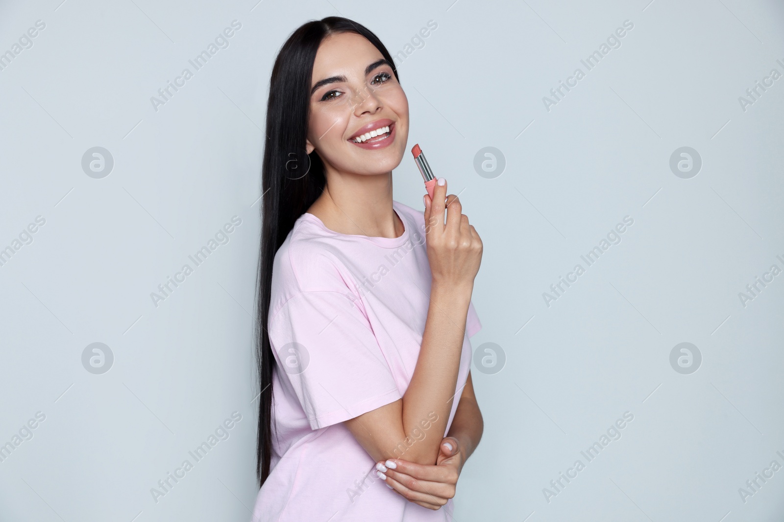 Photo of Young woman with beautiful makeup holding nude lipstick on light gray background