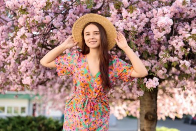 Photo of Beautiful woman in straw hat near blossoming tree on spring day