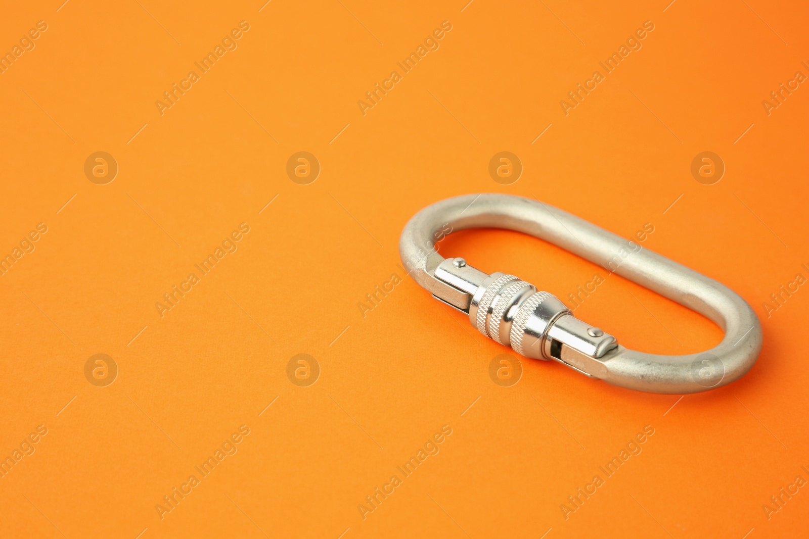 Photo of One metal carabiner on orange background, closeup. Space for text