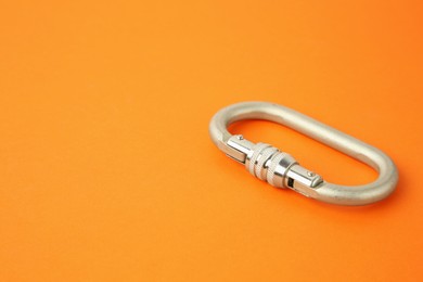 Photo of One metal carabiner on orange background, closeup. Space for text