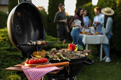 Photo of Group of friends having party outdoors. Focus on barbecue grill with food