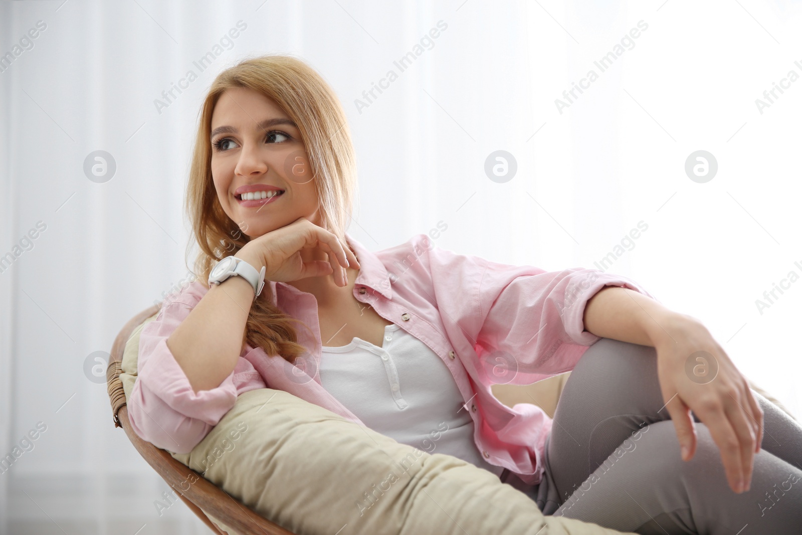 Photo of Young woman relaxing in papasan chair near window at home