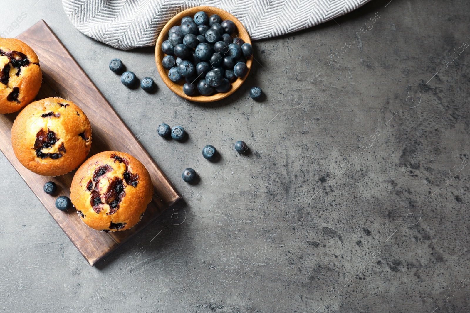 Photo of Wooden board with blueberry muffins on grey stone table, top view. Space for text