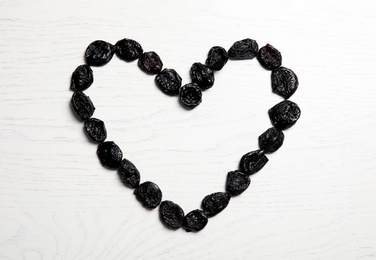 Photo of Heart shaped frame of sweet dried plums on wooden background, top view with space for text. Healthy fruit
