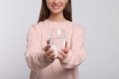 Photo of Healthy habit. Woman holding glass with fresh water against light grey background, focus on hands