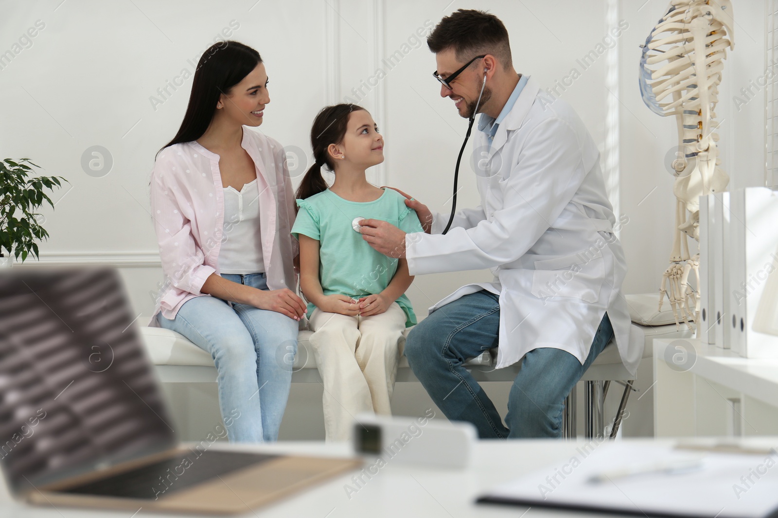 Photo of Mother with daughter visiting pediatrician in hospital. Doctor examining little girl