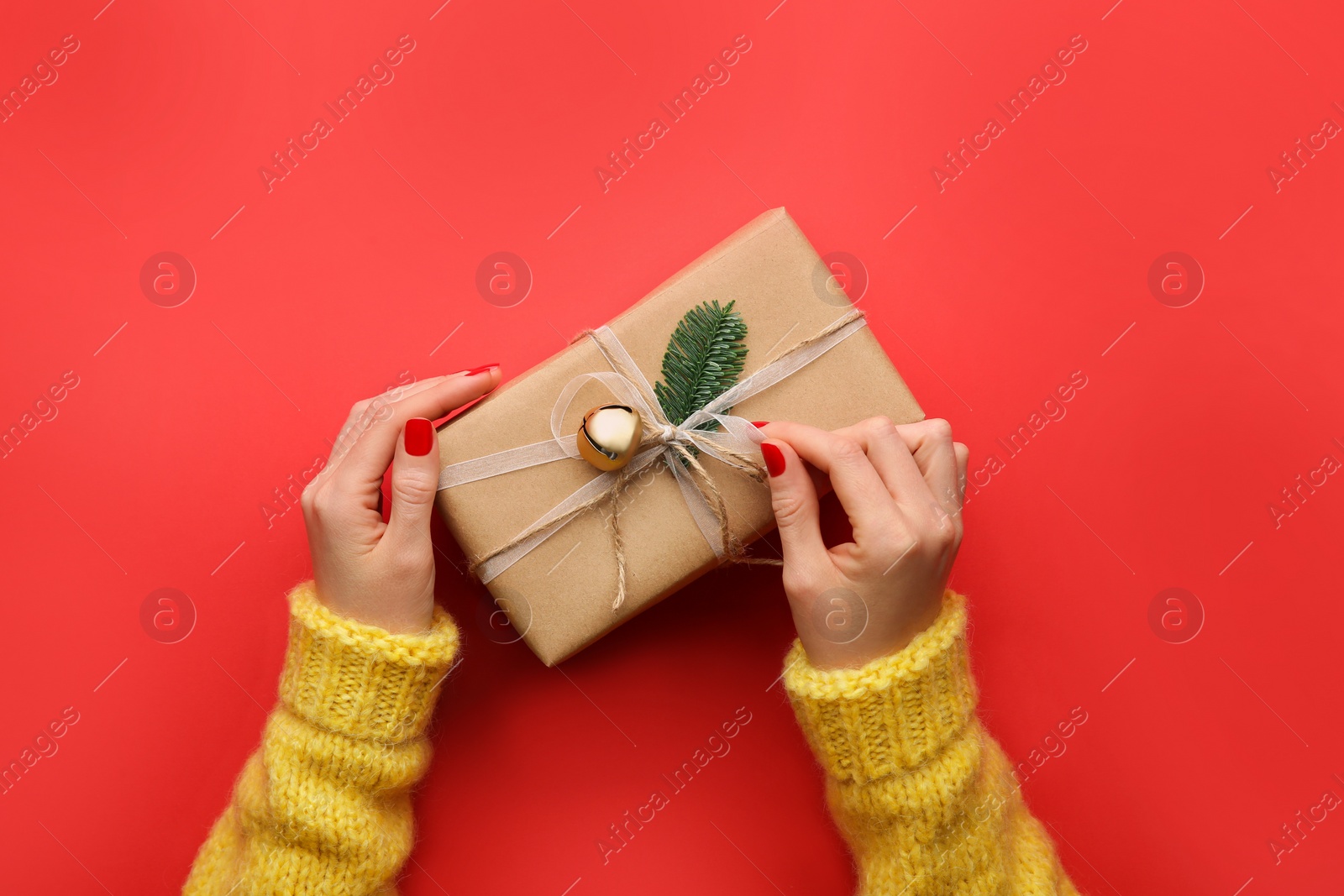 Photo of Woman holding Christmas gift box on red background, top view