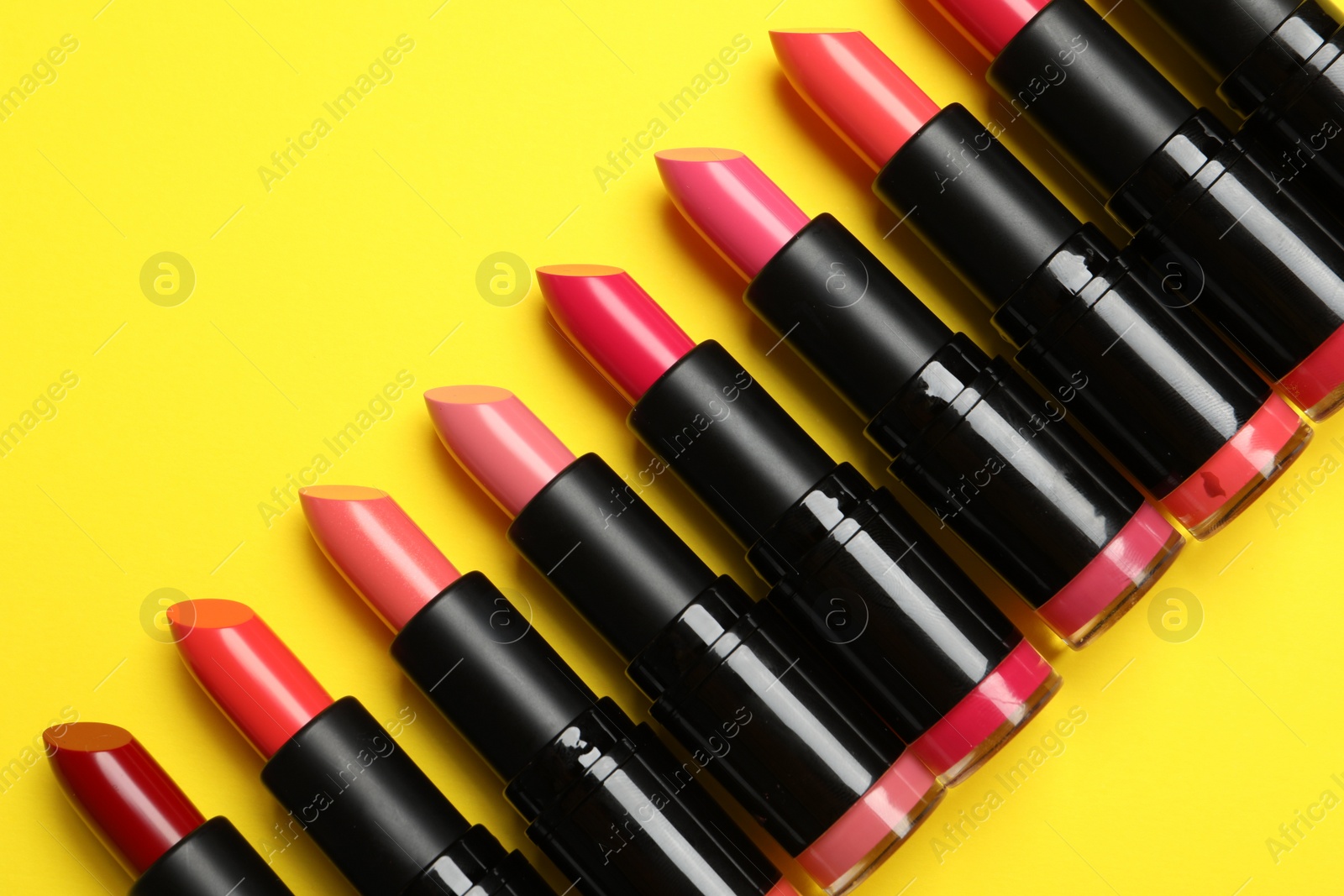 Photo of Many bright lipsticks on yellow background, flat lay