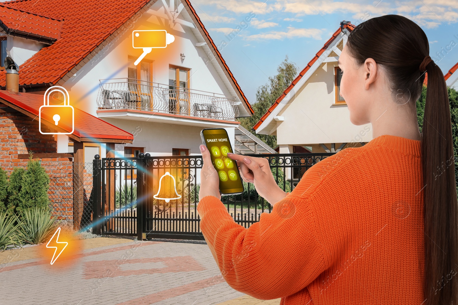 Image of Woman using smart home control system via application on mobile phone outdoors. Different icons on house