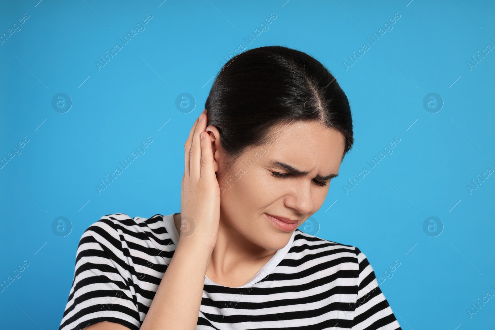 Photo of Young woman suffering from ear pain on light blue background