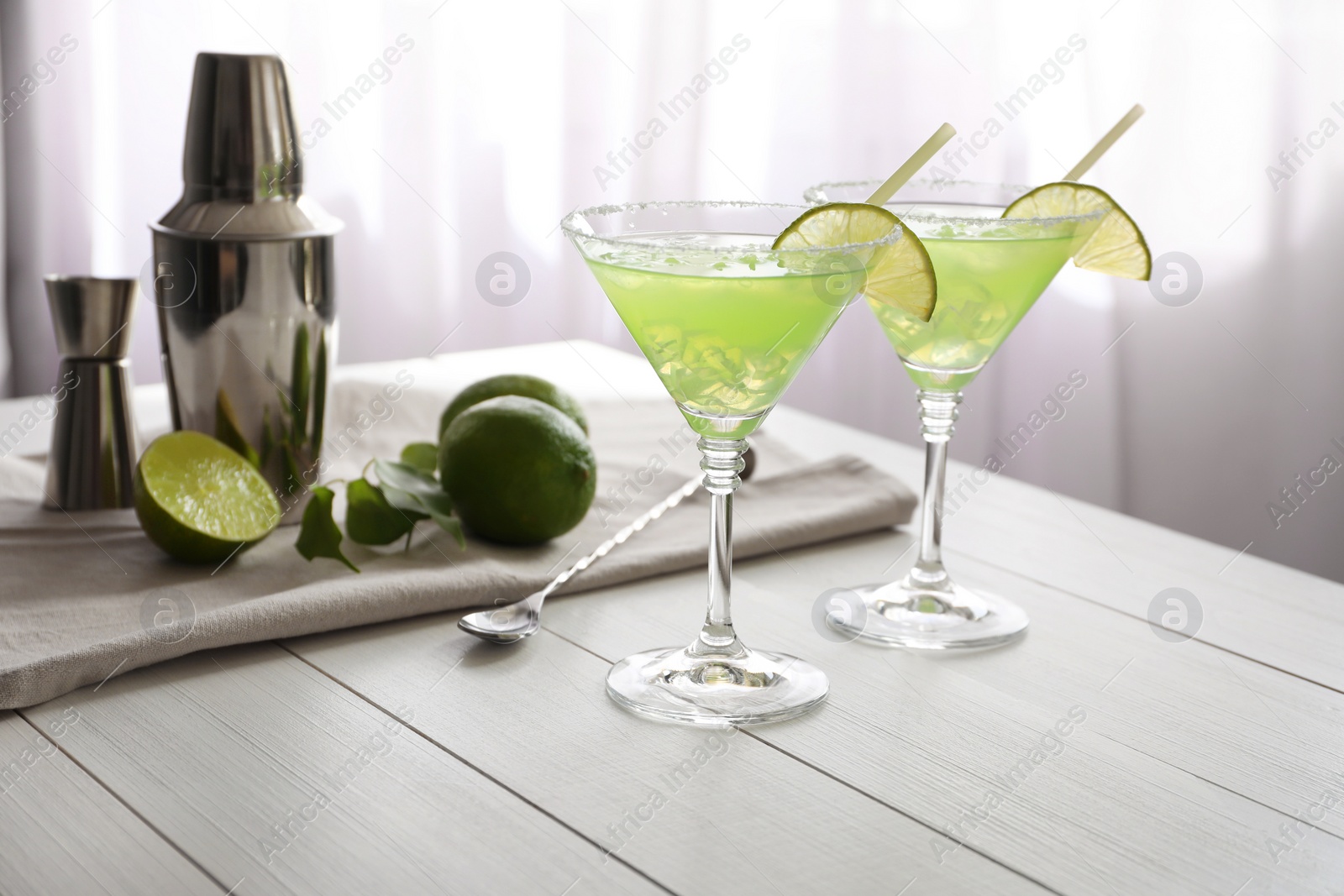 Photo of Delicious Margarita cocktail in glasses, limes and bartender equipment on white wooden table